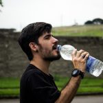 Person drinking water outdoors during a hot summer day