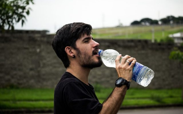 Person drinking water outdoors during a hot summer day